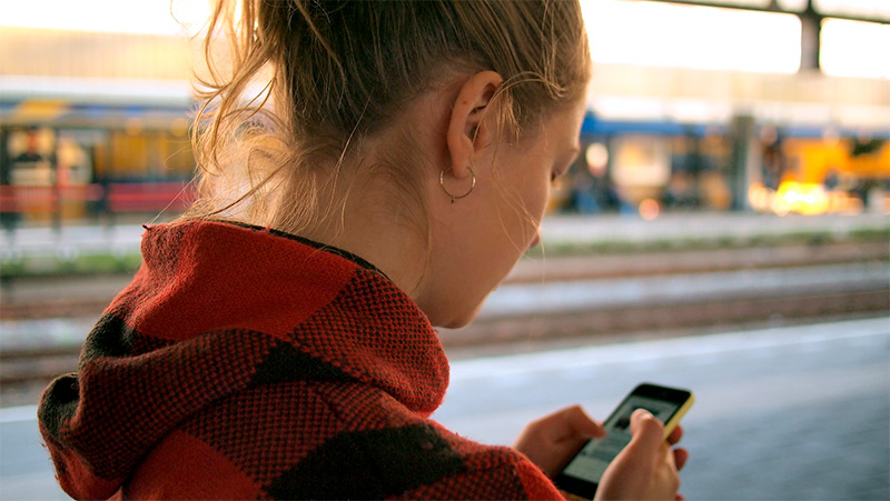 Nuori nainen käyttää puhelinta juna-asemalla