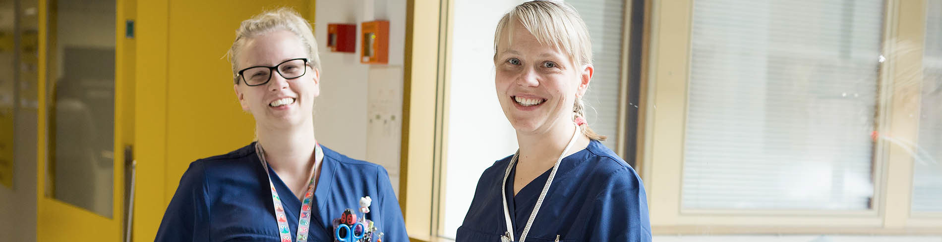 Kaksi vaaleaa hymyilevää hoitajaa Päijät-Hämeen keskussairaalassa.