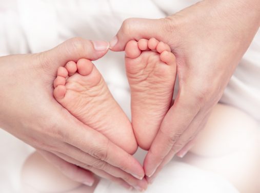 Äiti pitää käsissään vauvan jalkoja muodostaen sydän-kuvion